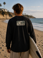 Wave Badge Long Sleeve Tee in black, back badge, walking to the water with a surfboard