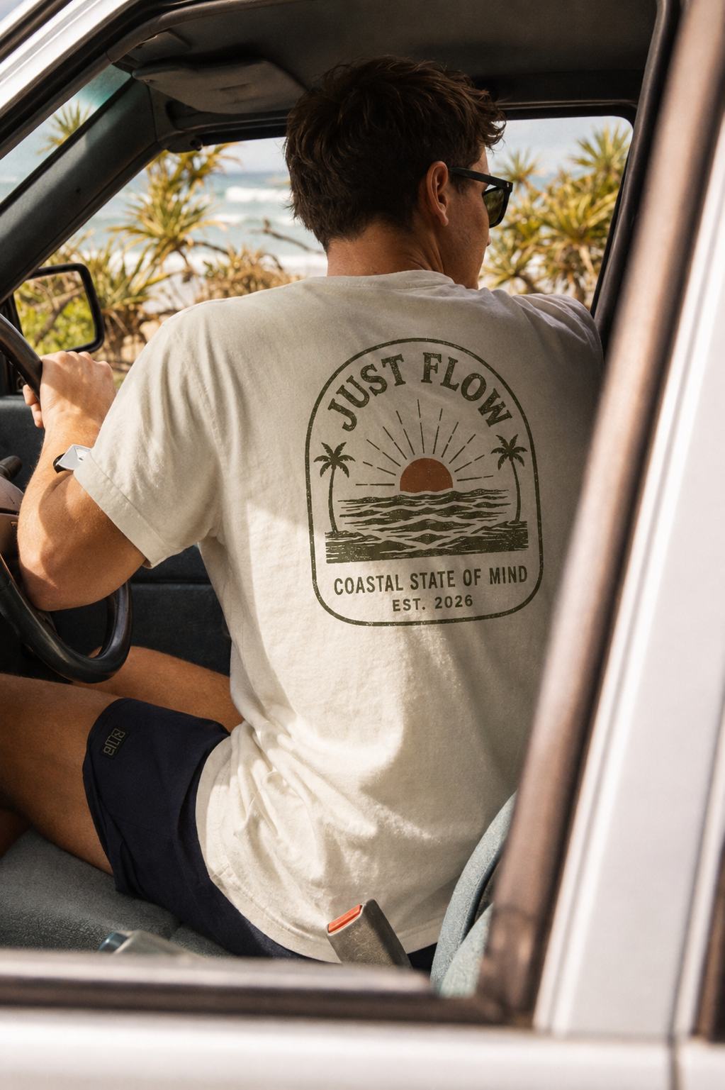 Coastal Sunset Heavyweight Tee in faded cream, back print, seen through a car window