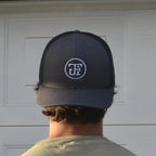 JFI Monogram Embroidered Trucker Cap in navy and black, worn, showing the stitched monogram