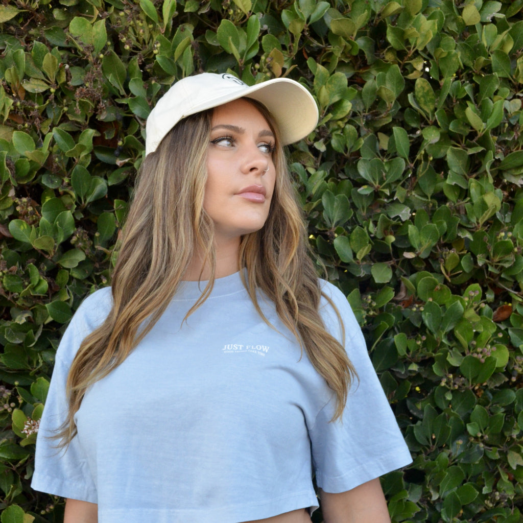 Minimal Wordmark Cropped Tee in periwinkle, worn with a Just Flow cap against a hedge in San Diego