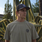 Circular Wave Crest Heavyweight Tee in sage, front logo worn in a San Diego agave garden