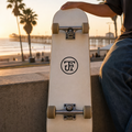 JFI Monogram sticker on an off-white skate deck, San Diego pier at sunset