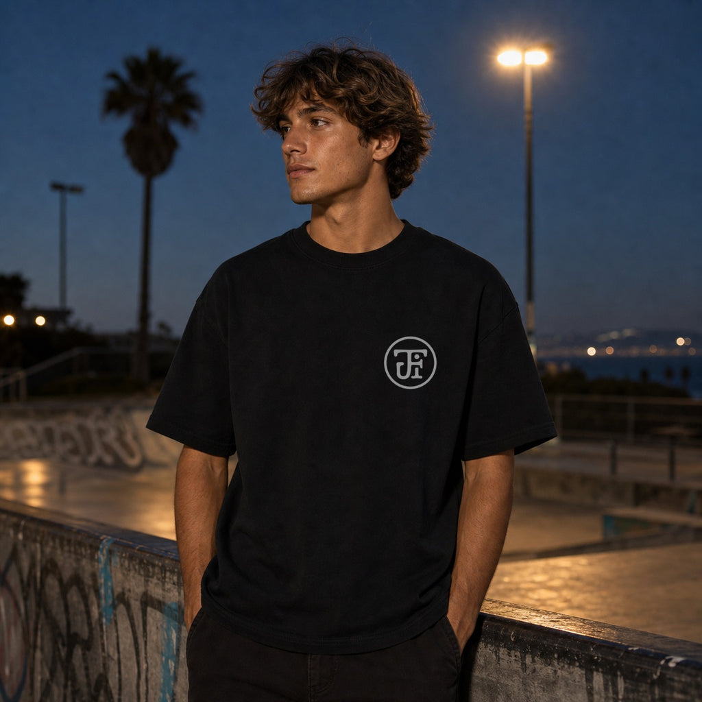 Monogram Heavyweight Tee in black — skate spot at dusk, white JFI monogram at the left chest